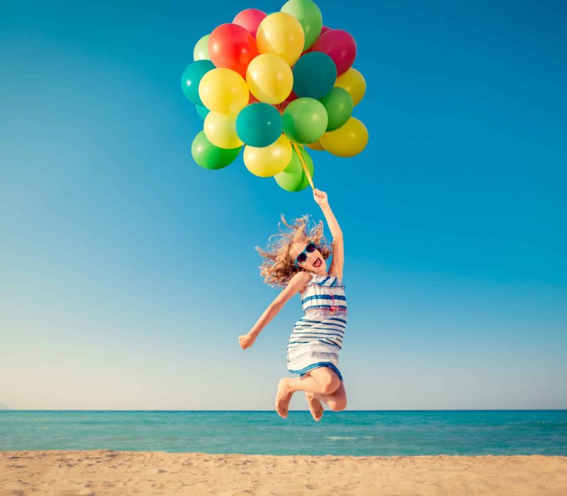 Happy,Child,Jumping,With,Colorful,Balloons,On,Sandy,Beach.,Portrait